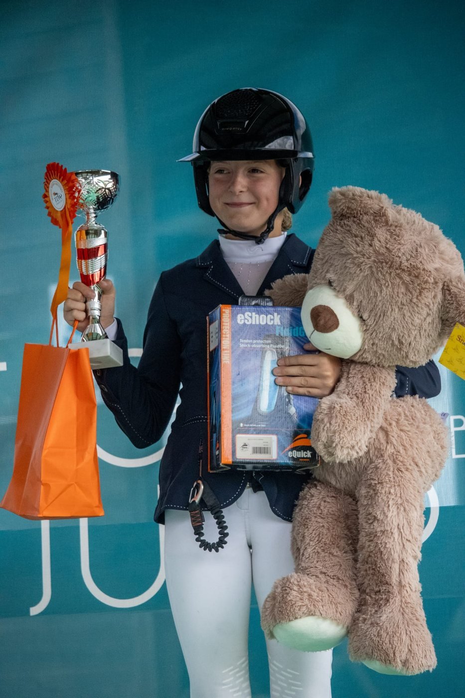 Jeune cavalière sur le podium avec sa coupe, son flot et ses lots